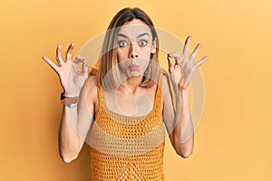 Young caucasian blonde woman wearing casual yellow t shirt looking surprised and shocked doing ok approval symbol with fingers