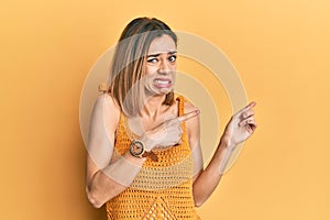 Young caucasian blonde woman wearing casual yellow t shirt pointing aside worried and nervous with both hands, concerned and