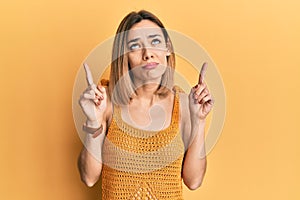 Young caucasian blonde woman wearing casual yellow t shirt pointing up looking sad and upset, indicating direction with fingers,