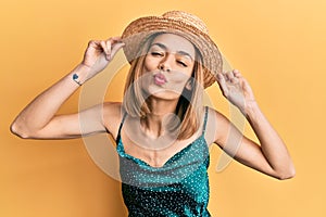 Young caucasian blonde woman wearing summer hat looking at the camera blowing a kiss being lovely and sexy