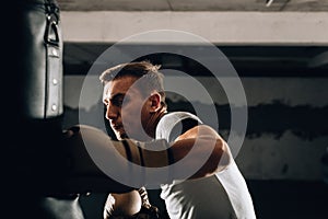 Young Caucasian boxer training alone with punching bag in health club