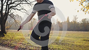 Young Caucasian boy in black sportswear jumping rope in the autumn park on sunset. Strong sportsman training outdoors