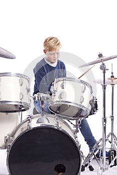 Young caucasian boy at drum kit in studio plays music