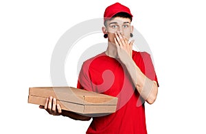 Young caucasian boy with ears dilation holding delivery pizza box covering mouth with hand, shocked and afraid for mistake