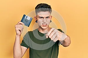 Young caucasian boy with ears dilation holding floppy disk annoyed and frustrated shouting with anger, yelling crazy with anger