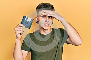 Young caucasian boy with ears dilation holding floppy disk stressed and frustrated with hand on head, surprised and angry face