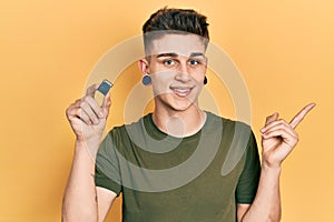 Young caucasian boy with ears dilation holding sdxc card smiling happy pointing with hand and finger to the side
