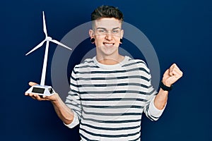 Young caucasian boy with ears dilation holding solar windmill for renewable electricity screaming proud, celebrating victory and