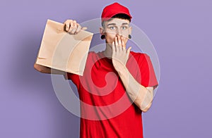 Young caucasian boy with ears dilation holding take away paper bag covering mouth with hand, shocked and afraid for mistake