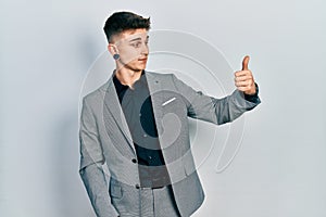 Young caucasian boy with ears dilation wearing business jacket looking proud, smiling doing thumbs up gesture to the side