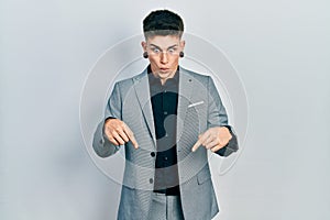 Young caucasian boy with ears dilation wearing business jacket pointing down with fingers showing advertisement, surprised face