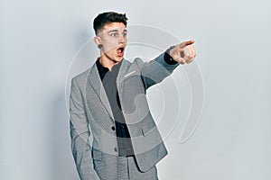 Young caucasian boy with ears dilation wearing business jacket pointing with finger surprised ahead, open mouth amazed expression,