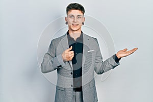 Young caucasian boy with ears dilation wearing business jacket showing palm hand and doing ok gesture with thumbs up, smiling