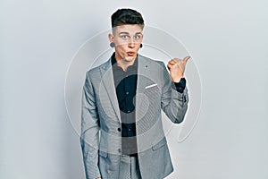 Young caucasian boy with ears dilation wearing business jacket surprised pointing with hand finger to the side, open mouth amazed