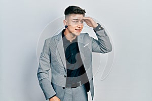 Young caucasian boy with ears dilation wearing business jacket very happy and smiling looking far away with hand over head