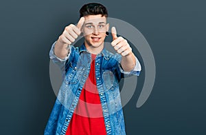 Young caucasian boy with ears dilation wearing casual denim jacket approving doing positive gesture with hand, thumbs up smiling