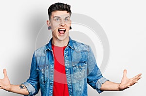 Young caucasian boy with ears dilation wearing casual denim jacket crazy and mad shouting and yelling with aggressive expression