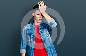 Young caucasian boy with ears dilation wearing casual denim jacket surprised with hand on head for mistake, remember error photo