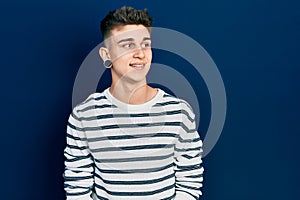 Young caucasian boy with ears dilation wearing casual striped shirt looking away to side with smile on face, natural expression