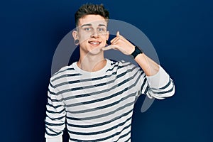 Young caucasian boy with ears dilation wearing casual striped shirt smiling doing phone gesture with hand and fingers like talking