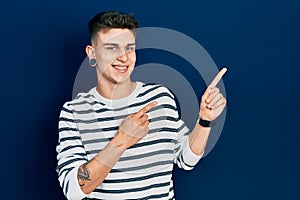 Young caucasian boy with ears dilation wearing casual striped shirt smiling and looking at the camera pointing with two hands and