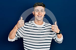 Young caucasian boy with ears dilation wearing casual striped shirt success sign doing positive gesture with hand, thumbs up