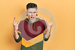Young caucasian boy with ears dilation wearing casual sweatshirt shouting with crazy expression doing rock symbol with hands up