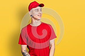 Young caucasian boy with ears dilation wearing delivery uniform and cap looking away to side with smile on face, natural