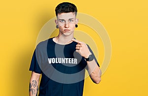 Young caucasian boy with ears dilation wearing volunteer t shirt pointing with hand finger to the side showing advertisement,