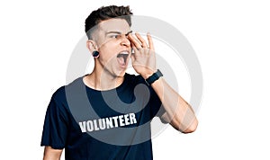 Young caucasian boy with ears dilation wearing volunteer t shirt shouting and screaming loud to side with hand on mouth