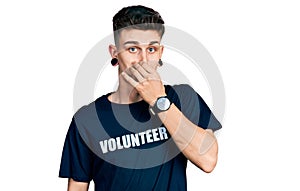 Young caucasian boy with ears dilation wearing volunteer t shirt smelling something stinky and disgusting, intolerable smell,