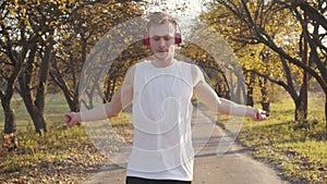 Young Caucasian boy in headphones and sportswear jumping rope in the autumn park. Athletic sportsman training outdoors