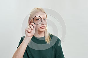 Young caucasian boy holding magnifying glass near eye