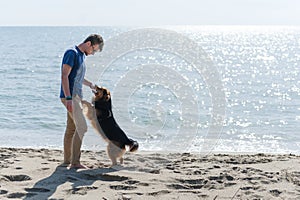 Young caucasian boy playing with dog on beach. Man and dog having fun on seaside