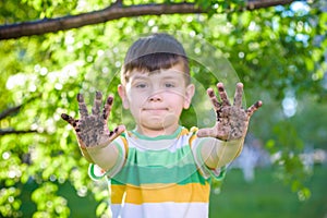 A young Caucasian boy showing off his dirty hands after playing in dirt and sand