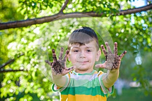 A young Caucasian boy showing off his dirty hands after playing in dirt and sand