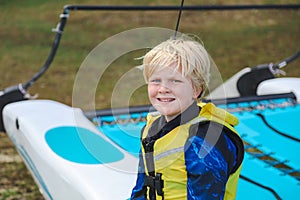 Young Caucasian boy wearing yellow life jacket sitting on boat ready to go sailing