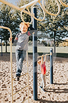 Young Caucasian boys friends hanging on monkey bars and pull-up bars in park on playground. Summer outdoor activity for kids.