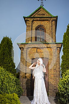 Young Caucasian Bride with Long White Hair Posing Against Old Brick Church Outdoors