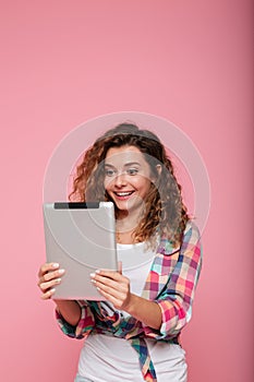 Young caucasian brunette lady using tablet computer isolated over pink