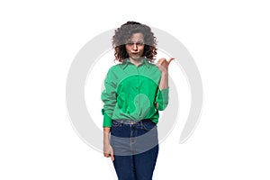 young caucasian brunette woman with curled hair dressed in a green shirt points her finger towards copy space