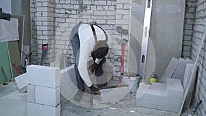 Young caucasian builder putting mortar on sides of aerated concrete block