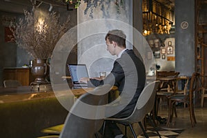 Young caucasian business man in formal suit working on laptop in a bar