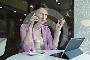 Young caucasian business woman is angry while talking on a mobile phone while sitting in a cafe with a cup of coffee
