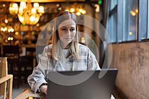 Young Caucasian business woman with blonde hair working on laptop in cafe. College student using technology , online