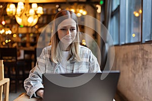 Young Caucasian business woman with blonde hair working on laptop in cafe. College student using technology , online