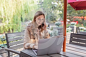 Young Caucasian business woman with blonde hair working on laptop in outdoor cafe. College student using technology