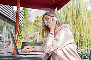 Young Caucasian business woman with blonde hair working on laptop in outdoor cafe. College student using technology