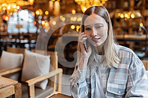 Young Caucasian business woman with blonde hair working on mobile phone in cafe. College student using technology