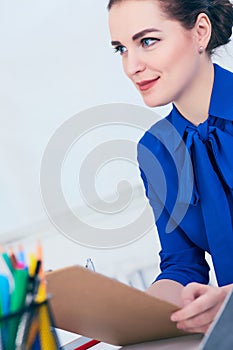 Young smiling business woman in jacket write on clipboard at the workplace in the office.